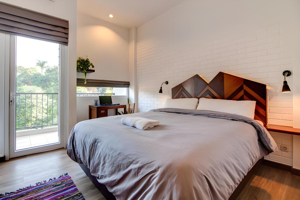 Kamar Studio dengan tempat tidur queen, dinding bata putih, dan pintu balkon menghadap pepohonan